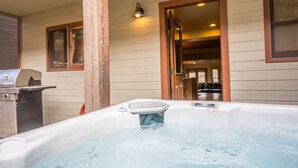 Un jacuzzi en el exterior de una casa, con una barbacoa cerca.