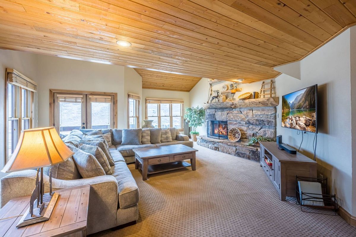 A cozy living room with a stone fireplace, a sofa set, a coffee table, and a television mounted on the wall.