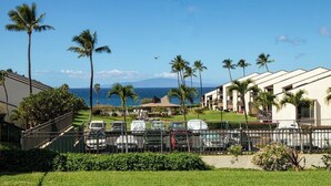 A hotel with a parking lot, palm trees, and a view of the ocean. - Hale Kamaole 152 Ground floor condo, easy access to best beach on Maui! (Kihei)