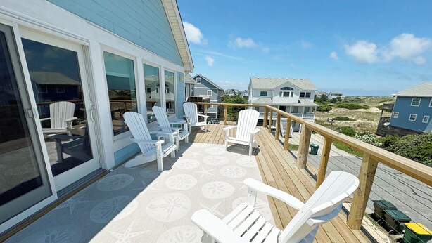 A deck with white Adirondack chairs, a wooden railing, and a view of the ocean and beach houses. - OS628- 4 Br. Oceanside with Pool, Hot tub, and Short walk to beach! (Corolla)
