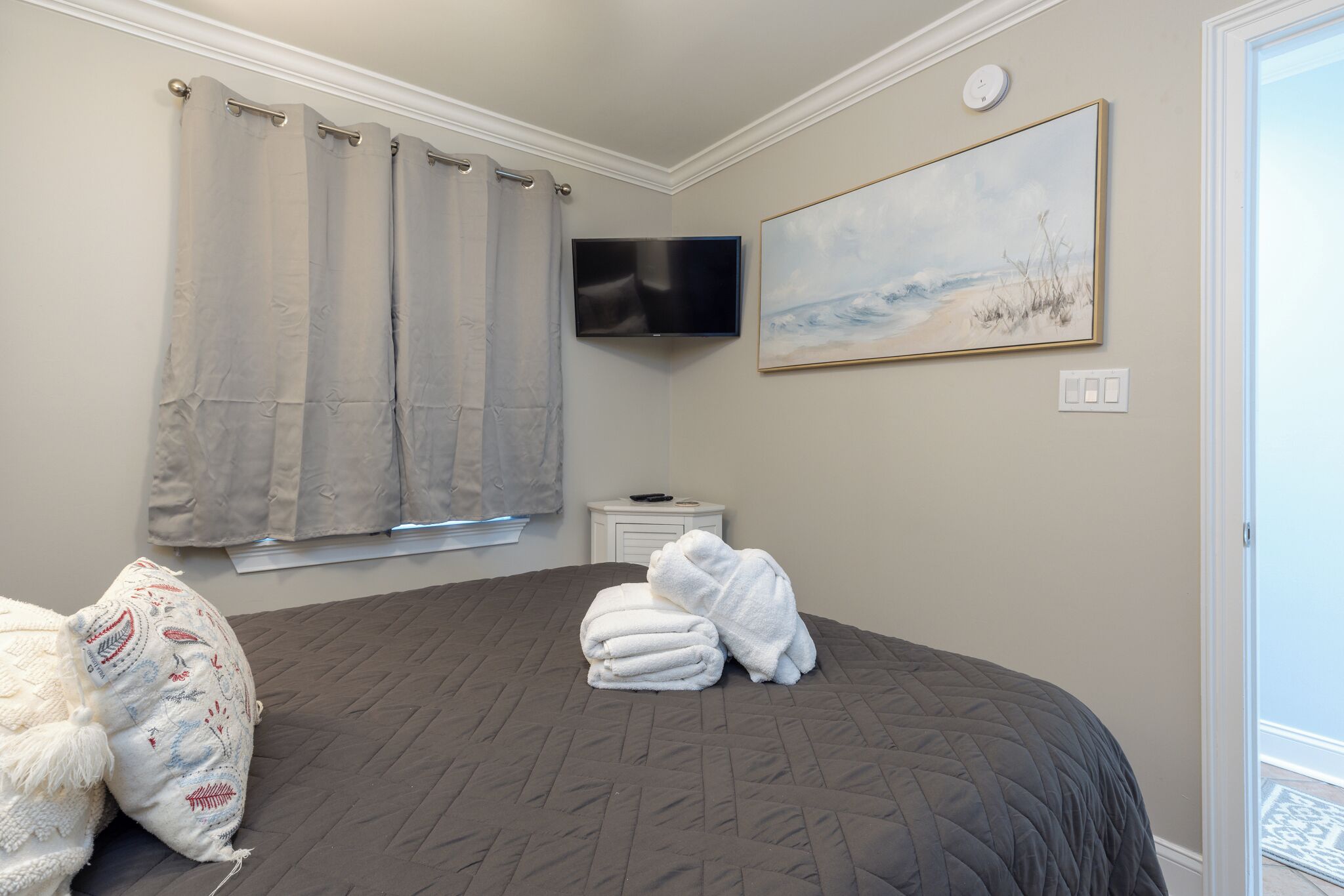 Ein Schlafzimmer mit einem Bett, einem Flachbildfernseher, einem Gemälde und einem Fenster mit Vorhängen.