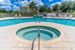 A swimming pool with a hot tub in the center, surrounded by lounge chairs and a fence.