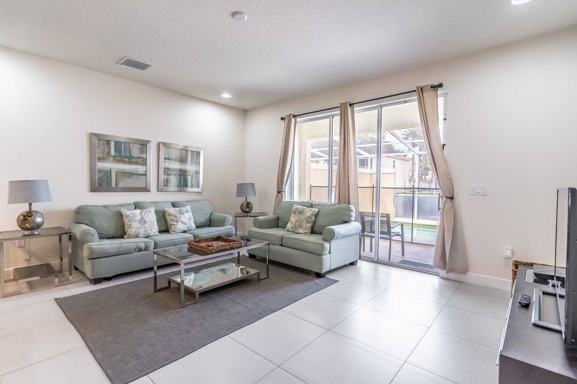 A living room with two sofas, a coffee table, and a TV. There are two lamps, a rug, and a window with curtains.