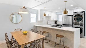 Une cuisine moderne avec des meubles blancs, un îlot central, des appareils en acier inoxydable et un coin repas avec des chaises en osier.