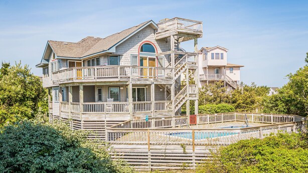 Une maison à plusieurs étages dotée d’un grand balcon, d’une piscine et d’un escalier menant aux niveaux supérieurs.