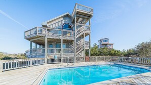 Un espace aménagé au bord de la piscine, doté d’une terrasse en bois, d’une piscine à l’eau cristalline et d’une structure en bois à plusieurs niveaux, agrémentée de balcons.