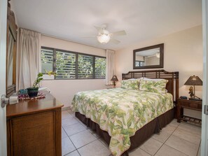 A bedroom with a bed, a ceiling fan, a window with curtains, a bedside table, and a nightstand.