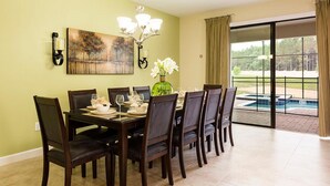 Un coin repas avec une table dressée pour six personnes, des chaises, un lustre, un tableau et une vue sur une piscine.