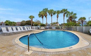 A circular pool with a metal ladder, surrounded by lounge chairs and palm trees.
