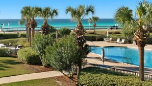 A pool area with palm trees, a view of the ocean, and a paved walkway. - Two Balconies, Gorgeous Views of the Gulf, Beachy Flair (Miramar Beach)