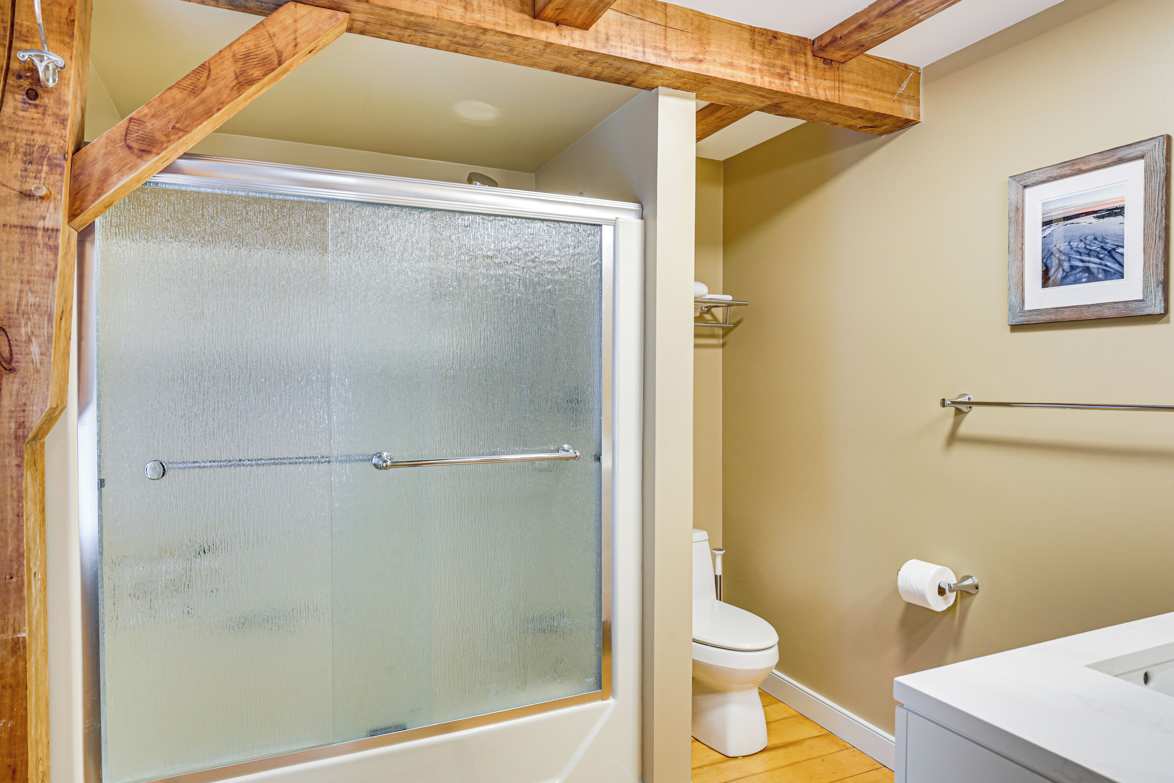 A bathroom with a glass-enclosed shower, a toilet, and a framed picture on the wall.