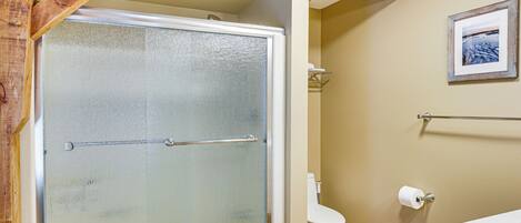 A bathroom with a glass-enclosed shower, a toilet, and a framed picture on the wall.
