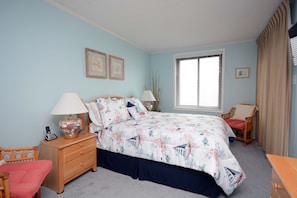 A bedroom with a bed, nightstand, chair, and a window with blinds.