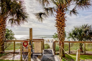 A wooden deck leading to a beach with palm trees, a pool rules sign, and a view of the ocean.