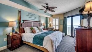 A neatly arranged bedroom with a bed, bedside tables, a ceiling fan, and a view of the outdoors through a window. - 🏖️Stunning Ocean Views | Pools + Hot Tub | The Island 710/720🏖️ (Myrtle Beach)