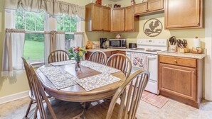 A kitchen with wooden cabinets, a dining table with chairs, a microwave, a stove, and various kitchen utensils. - 'Grandma's Farm House' on 125 Acres w/ Fire Pit! (Beattyville)