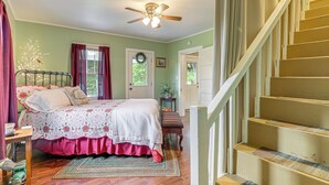 A bedroom with a bed, a wooden floor, a ceiling fan, a staircase, and a door with a wreath. - 'Grandma's Farm House' on 125 Acres w/ Fire Pit! (Beattyville)