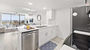 A modern kitchen with a dishwasher, double sink, and black stove. - Direct Oceanfront Newly Renovated Condo w/ Private Balcony (Cape Canaveral)
