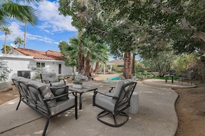 Un patio al aire libre con un comedor, una piscina y palmeras.