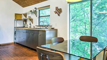 A modern kitchen with a large window, wooden ceiling, and a dining area with a glass table and chairs.