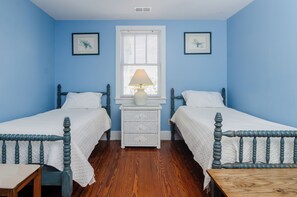 A room with two beds, a nightstand with a lamp, and a window with blinds.