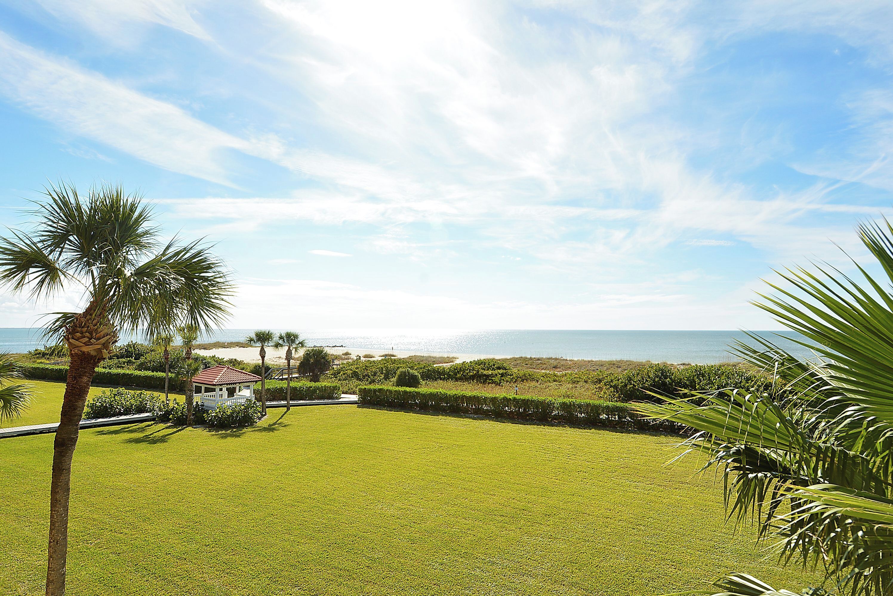A well-maintained lawn with a small building, palm trees, and a view of the ocean.