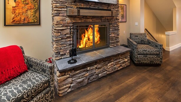 Una sala de estar con chimenea de piedra, televisor montado encima y sofá con una manta roja.