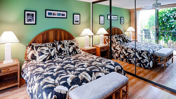 Ein Hotelzimmer mit einem großen Bett, zwei Nachttischen, einer Bank und einem großen Spiegel, der den Raum reflektiert.