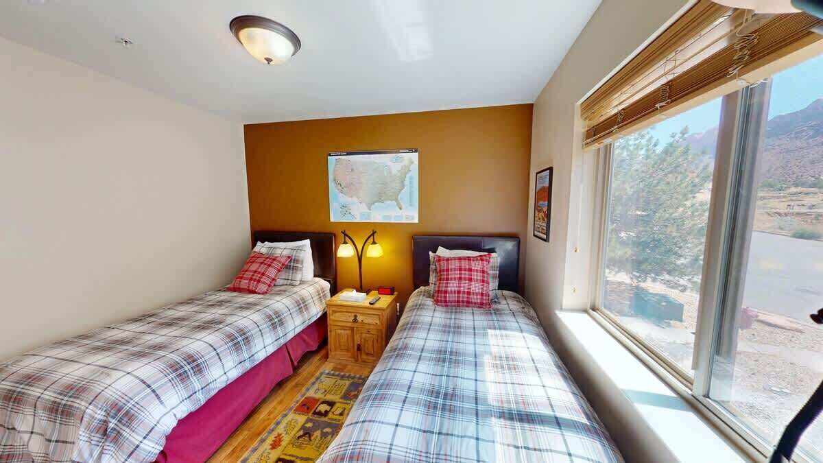 A room with two beds, a map on the wall, a window with a view, and a small wooden table.
