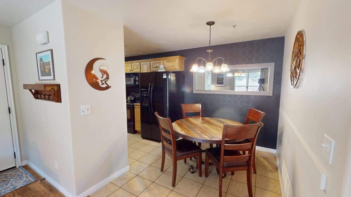A dining area with a round table and chairs, a kitchen with dark cabinetry, and a wall-mounted light fixture.
