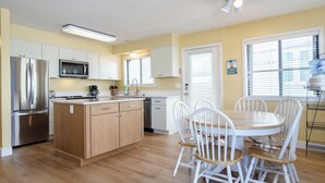 A modern kitchen with stainless steel appliances, wooden cabinets, and a dining area with white chairs.
