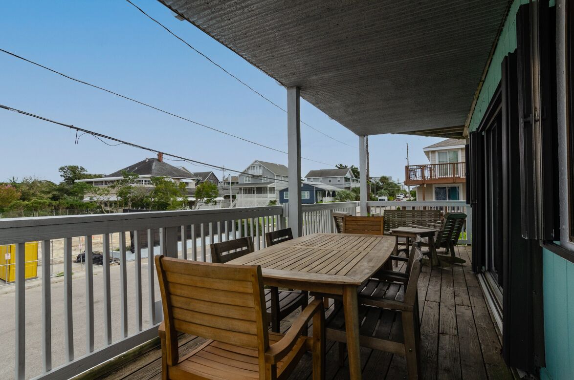 A wooden deck with tables and chairs, overlooking a residential area with houses and a clear sky.