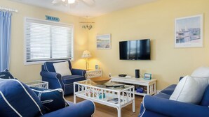 A living room with a ceiling fan, a TV, a sofa, a coffee table, and a window with blinds.