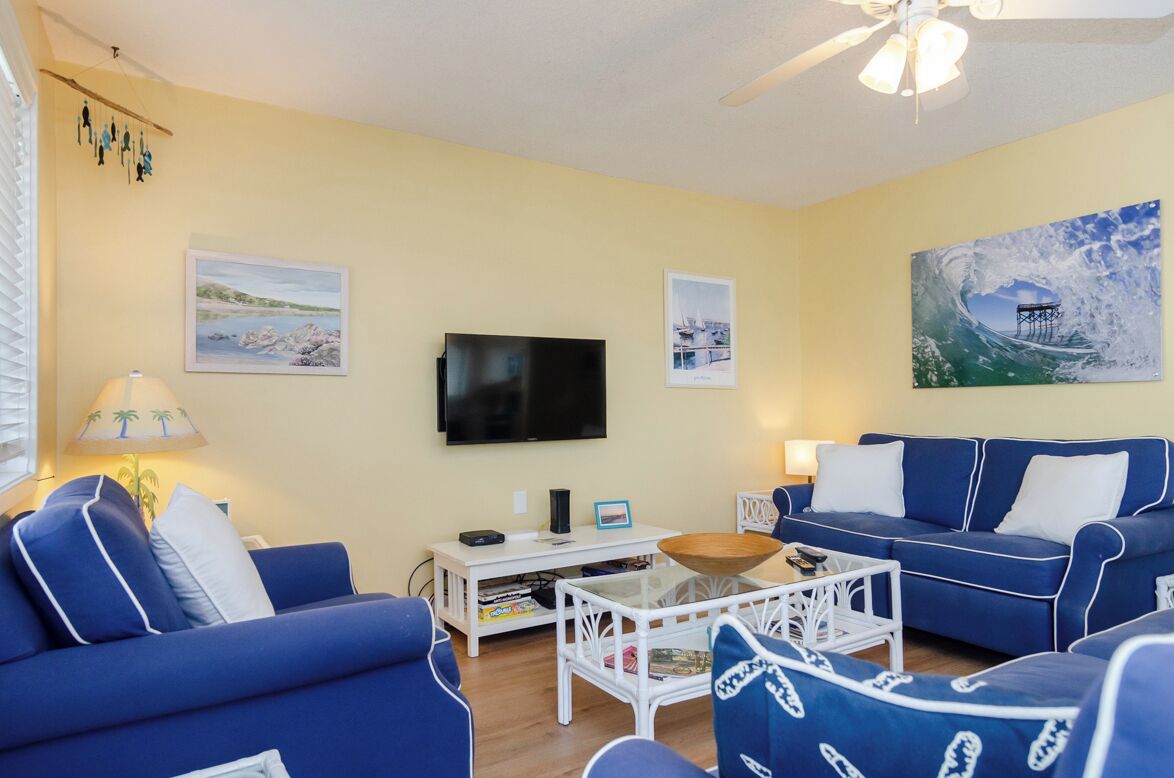 A living room with a blue sofa, a white coffee table, and a flat-screen TV mounted on the wall.
