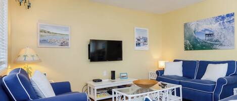 A living room with a blue sofa, a white coffee table, and a flat-screen TV mounted on the wall.