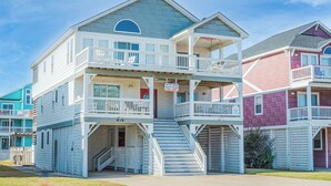 A multi-story beach house with balconies, a staircase, and a 'Rent' sign.