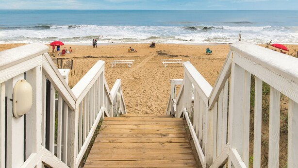 A wooden staircase leading to a sandy beach with a view of the ocean.