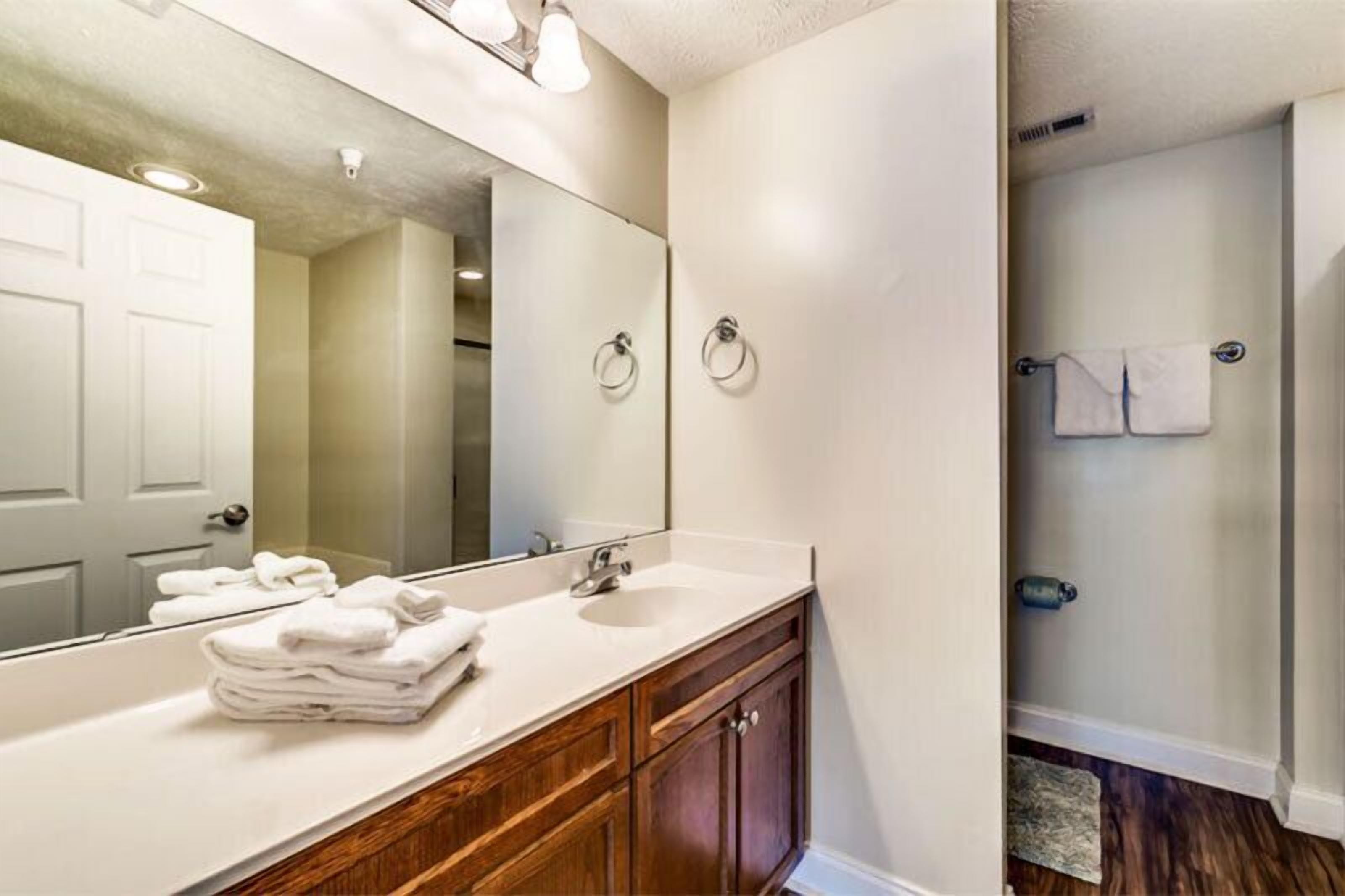 A bathroom with a white sink, wooden vanity, and a large mirror.