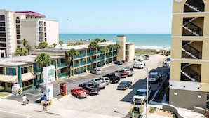 Un hôtel à plusieurs étages doté d’un parking, offrant une vue sur la plage et arborant une enseigne indiquant la présence d’un restaurant.