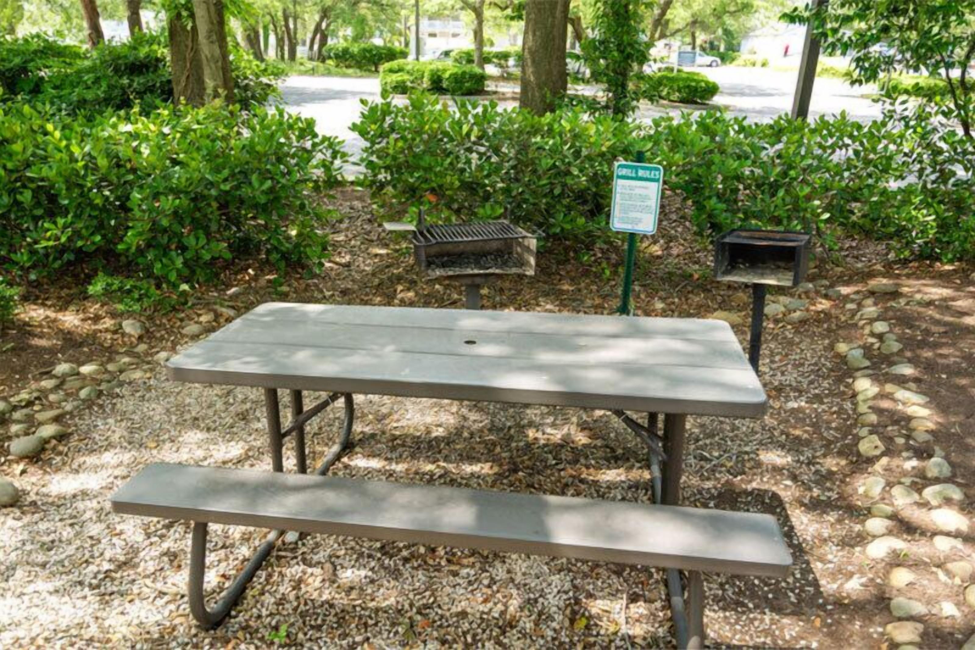 A picnic table with a grill in a park area.