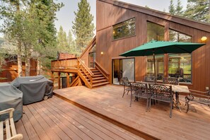 Une terrasse en bois avec des meubles d’extérieur, un barbecue couvert et un escalier menant à une autre terrasse.