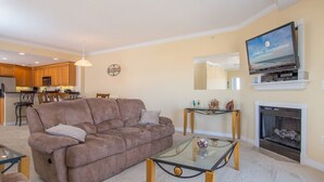 Una sala de estar con un sofá marrón, una mesa de centro de vidrio, una chimenea y un televisor sobre un mueble.