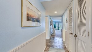 A hallway with a framed picture on the wall, a patterned rug, and white doors with louvered tops.