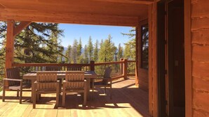 A wooden deck with a table and chairs, overlooking a forested area. - Spectacular Mountain Home with Spacious Living Areas (Whitefish)