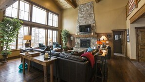 A spacious living room with a stone fireplace, leather sofa, and large windows. - Spectacular Mountain Home with Spacious Living Areas (Whitefish)