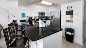 A modern kitchen with white cabinets, a black countertop, stainless steel appliances, and a dining area with wooden chairs.