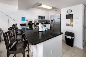 A modern kitchen with white cabinets, a black countertop, stainless steel appliances, and a dining area with wooden chairs.