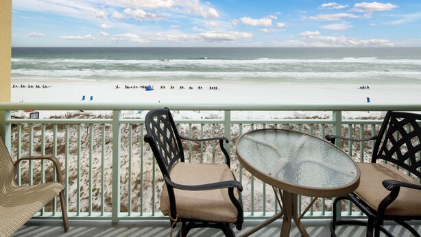 A balcony with a view of the beach, featuring two chairs and a table.