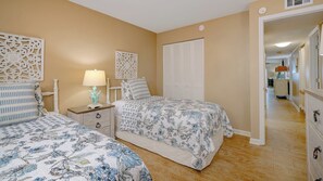 A bedroom with two beds, a nightstand, a lamp, and a wardrobe. - Coastal Luxury on the Gulf | Pool, Tennis & Trolley Beachfront Bliss on Anna Maria Island | Sleeps 6 (Holmes Beach)