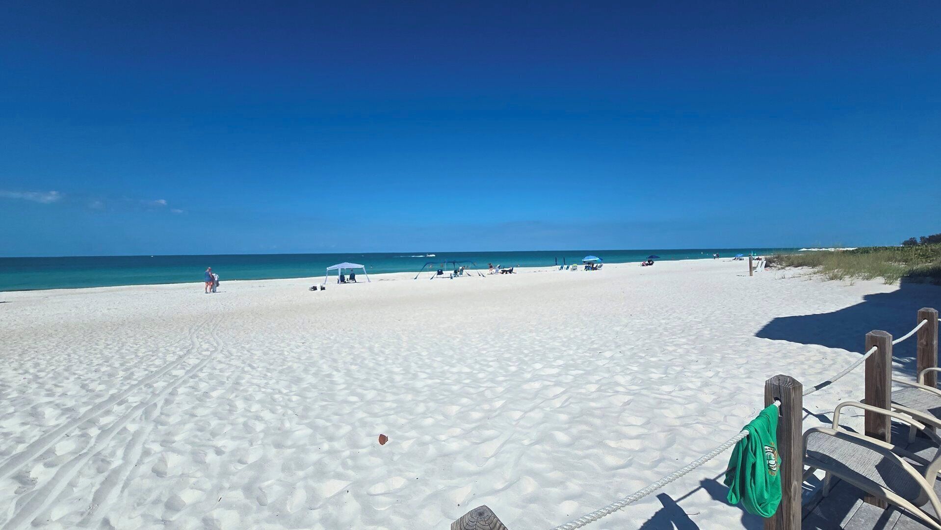 Ein Strand mit weißem Sand, klarem blauen Wasser und einigen Sonnenschirmen.